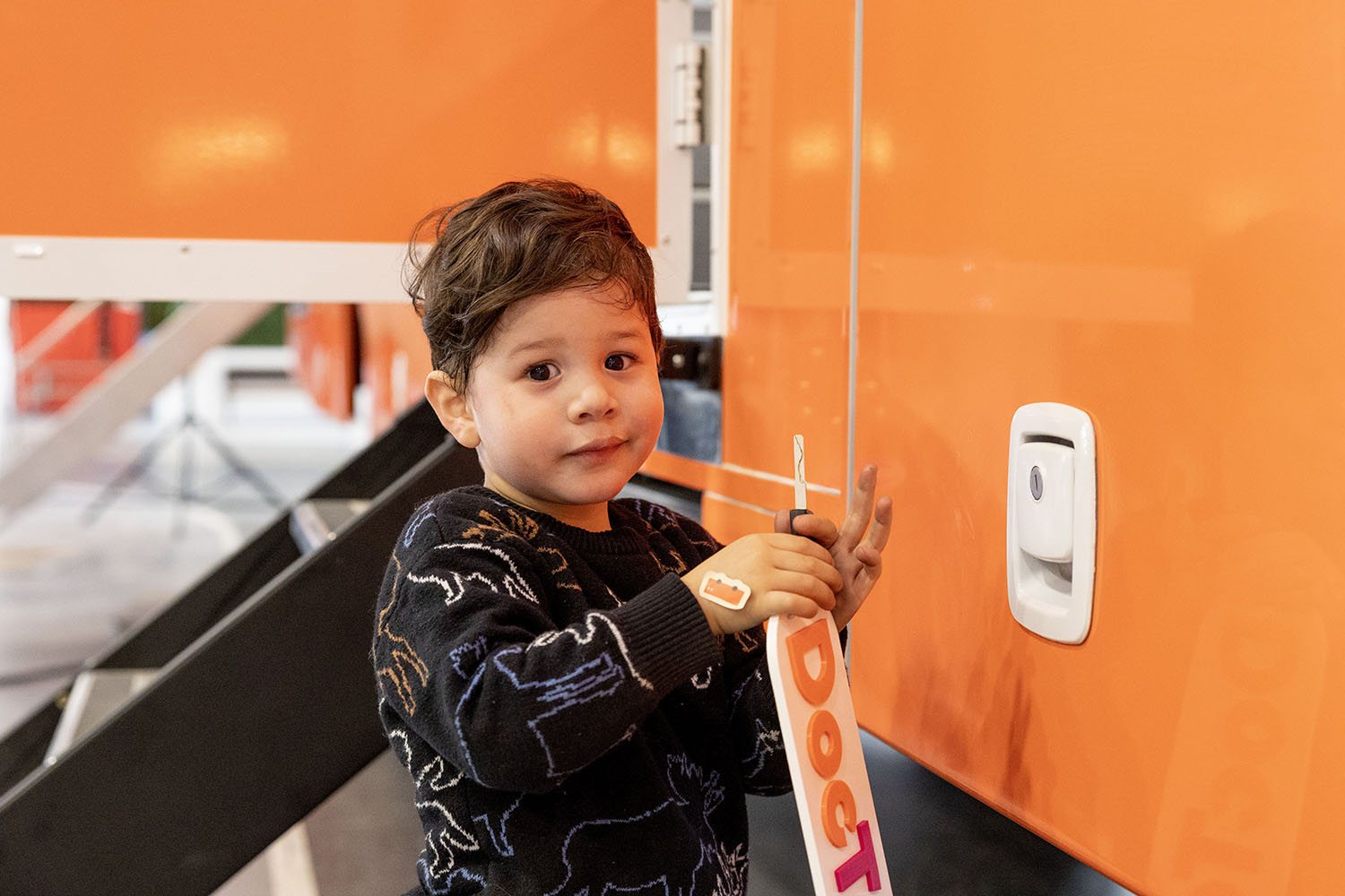 Un jeune enfant pose la main sur la carrosserie orange de la clinique mobile
